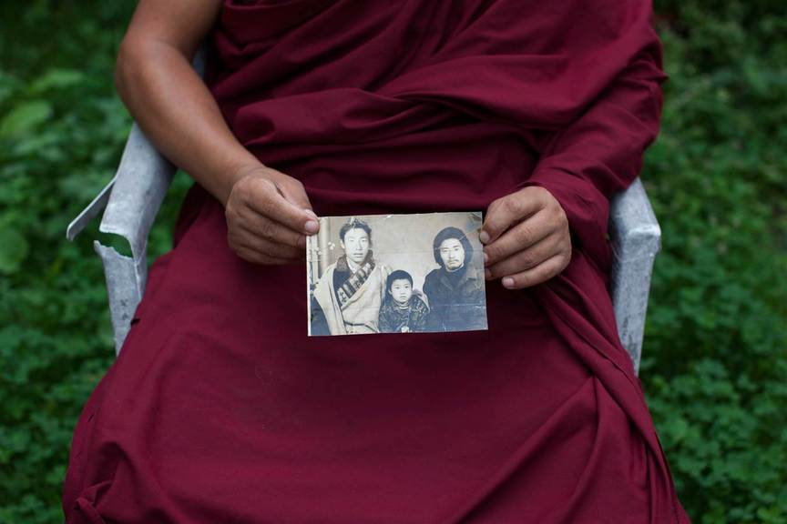 Tibetan monk Dorjee, 38, displays a photograph of his father, left, and himself, center. Dorjee said he held back his tears when he spoke with his parents on the phone after 27 years apart. He exchanged a few words with his father but says his mother fainted when she heard his voice. Copyright the artist.