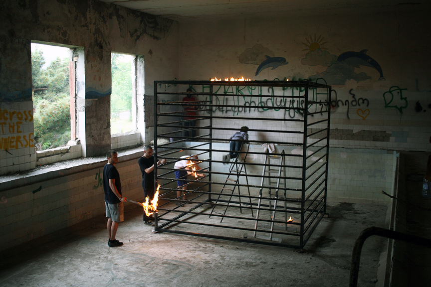 Students trying to set a metal cage sculpture on fire in the former pool.