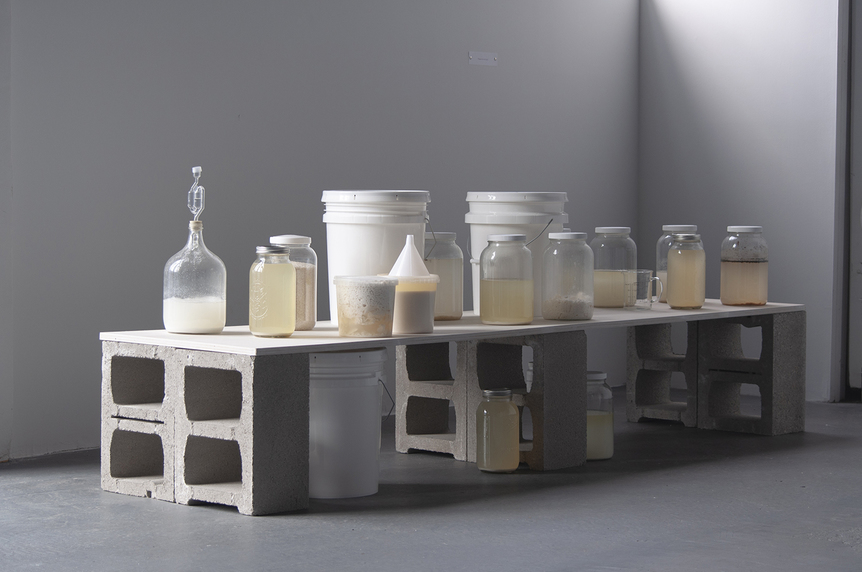 Installation view of TIFFANY JAEYEON SHIN’s Untitled (Lactic Acid Brew), 2018, wood, cinder blocks, glass jars, mason jars, food grade container, funnel, homebrewed lactic acid, 243.8 × 61 × 61 cm, at “Universal Skin Salvation,” Knockdown Center, New York, 2018.