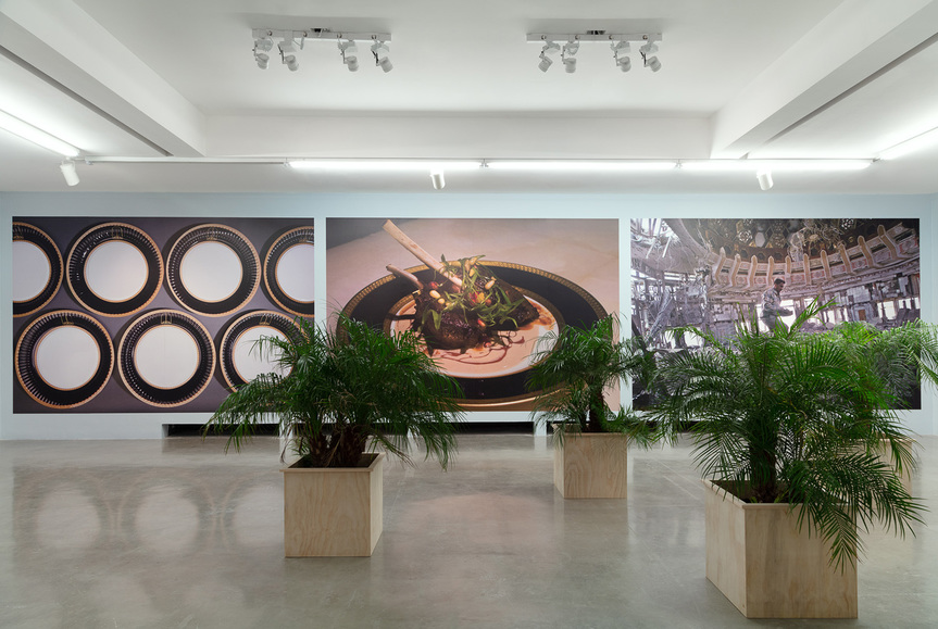 Partial installation view of MICHAEL RAKOWITZ’s Spoils, 2011, culinary intervention and mixed-media installation with digital wallpaper, digital color video with sound: 9 min 55 sec, printed paper plates, framed copy of the New York Times, dimensions variable, at “Dispute Between the Tamarisk and the Date Palm,” REDCAT, Los Angeles, 2019. Courtesy the artist and Rhona Hoffman Gallery, Chicago.