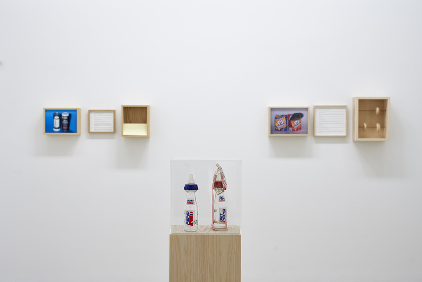 Installation view of MARYAM JAFRI’s Product Recall: An Index of Innovation (Pepsi Baby Bottle), 2014-15, Pepsi baby bottles (plastic/cardboard), plinth, framed text, dimensions variable, at “Roads to Serfdom, Repaved,” Taxispalais Kunsthalle Tirol, 2019. Photo by Günter Kresser.