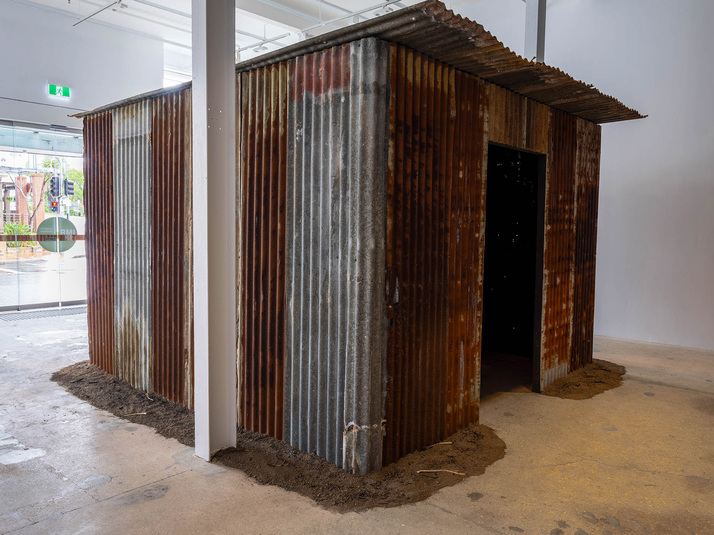 Installation view of SANCINTYA MOHINI SIMPSON’s Kortri, 2020, corrugated iron structure, wooden bench, soil, scent, dimensions variable, at "Kūlī nām dharāyā / they’ve given you the name ‘coolie’,” IMA Belltower, Brisbane, 2020. Photo by Carl Warner. Courtesy IMA, Brisbane.