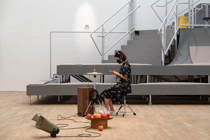 Installation view of “trust and confusion” at Tai Kwun Contemporary with YUKO MOHRI‘s Decomposition, 2021, apple, seasonal fruits, wooden dish, computer, audio amplifier, and speaker, in the foreground and TAREK ATOUI’s Whisperer, 2021, mixer, amplifier, microphone piezo, transducer, two wooden boxes, brass rod, and cymbal, in the background.